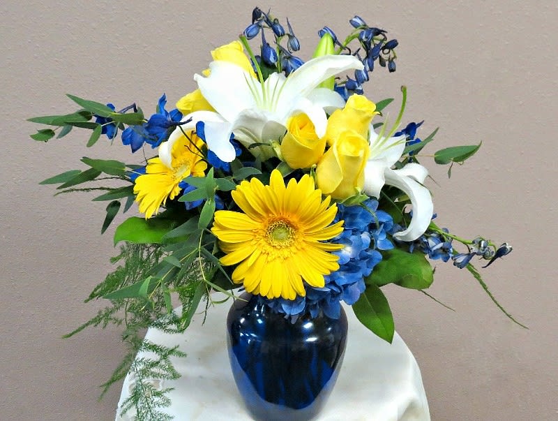 Bouquet of yellow roses, white lilies, and blue flowers in a dark vase