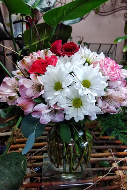 Mixed bouquet of white daisies, pink alstroemeria, and red roses in a glass vase