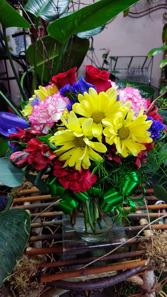 Mixed bouquet with yellow daisies, red roses, and pink carnations in a glass vase
