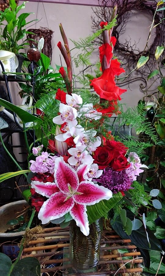 Tall mixed floral arrangement with red roses, pink lilies, and white orchids in a glass vase