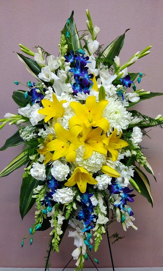Tall floral standing spray with yellow lilies, white blooms, and blue orchids