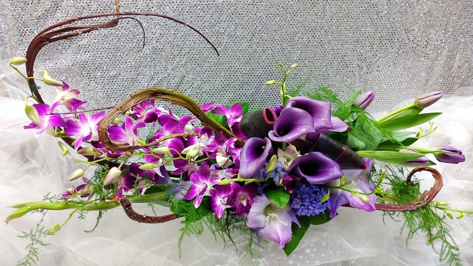 Long modern centerpiece of purple calla lilies and orchids with curved vine accents