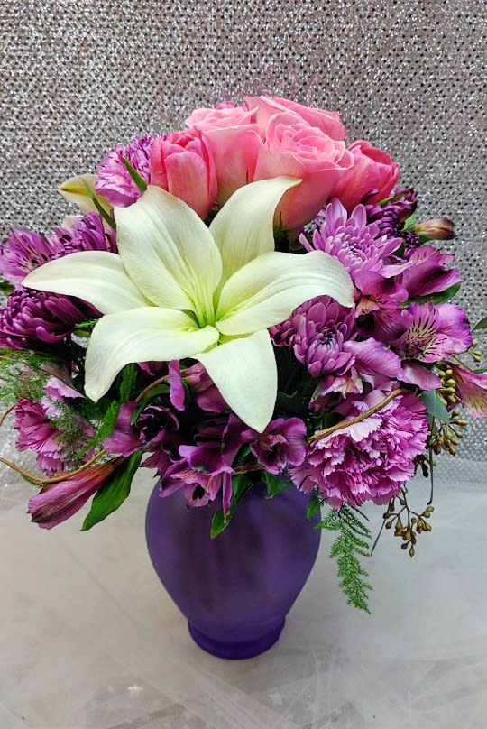 Pink roses and purple flowers arranged in a purple vase with a white lily