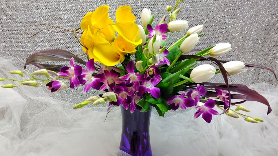 Yellow calla lilies and purple orchids in a purple vase