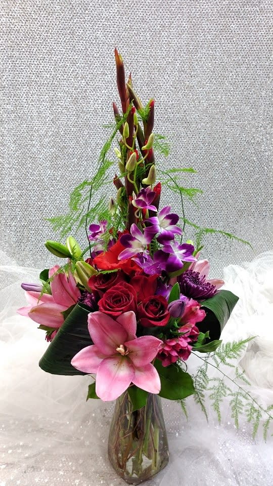 Tall bouquet of pink lilies, red roses, and purple orchids in a glass vase