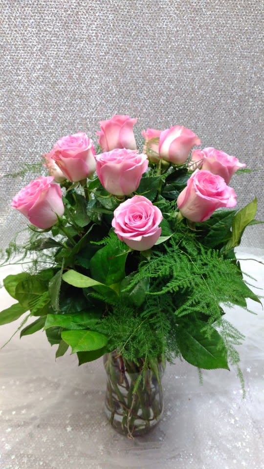 Pink roses arranged in a clear glass vase with greenery