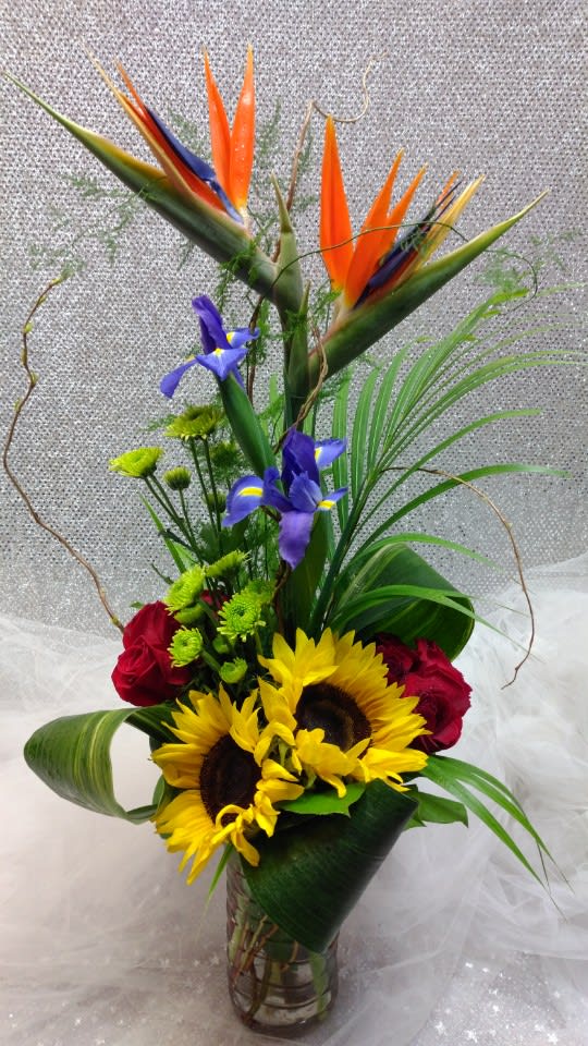 Tropical bouquet with sunflowers, red roses, and bird of paradise in a glass vase
