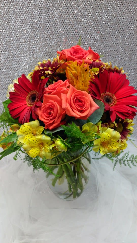 Bouquet of red gerbera daisies, coral roses, and yellow alstroemeria in a glass vase
