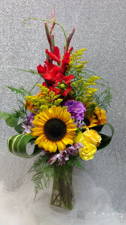 Tall mixed bouquet with sunflowers, red gladiolus, and yellow roses in a clear vase