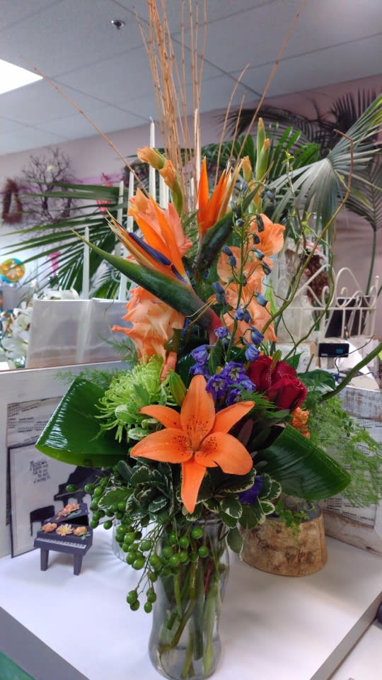 Tall tropical bouquet with orange lilies and purple accents in a glass vase