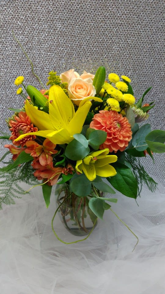 Mixed bouquet with yellow lilies, peach roses, and orange blooms in a glass vase