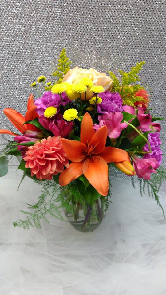 Colorful bouquet with orange lilies, pink flowers, and yellow blooms in a glass vase