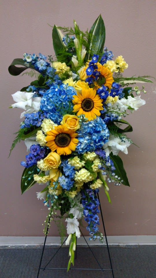 Tall standing floral spray with sunflowers, blue hydrangeas, and white blooms