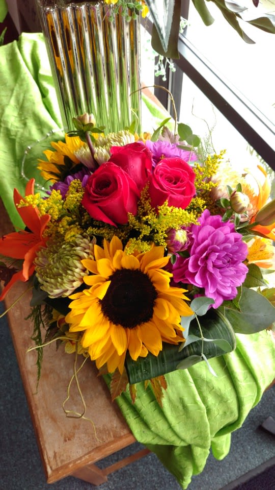 Bouquet of red roses, sunflowers, and purple blooms in a vase