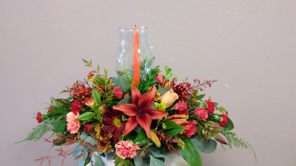 Mixed floral arrangement in a clear glass vase with an orange candle
