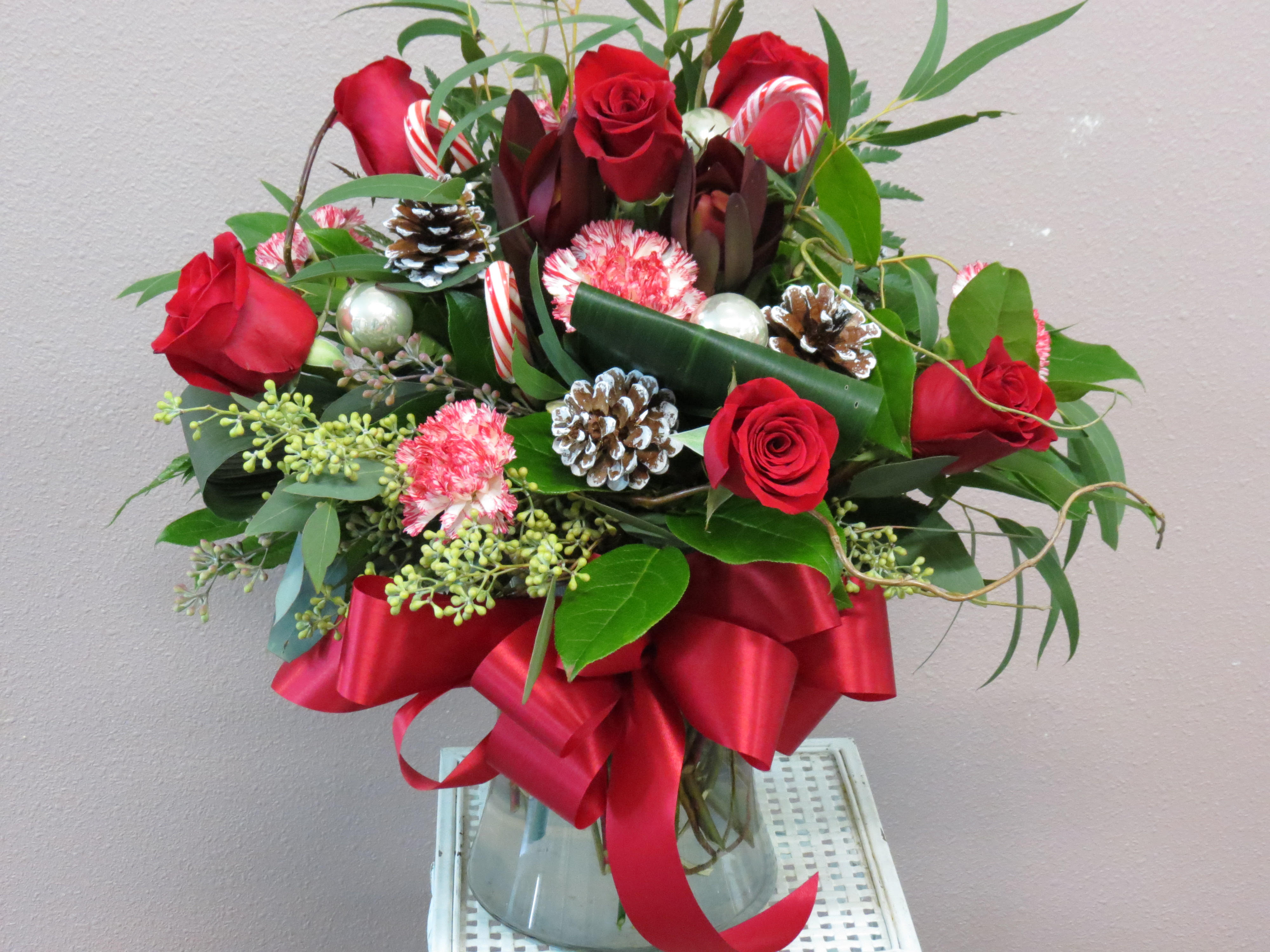 Red roses and candy canes arranged in a glass vase with a red ribbon