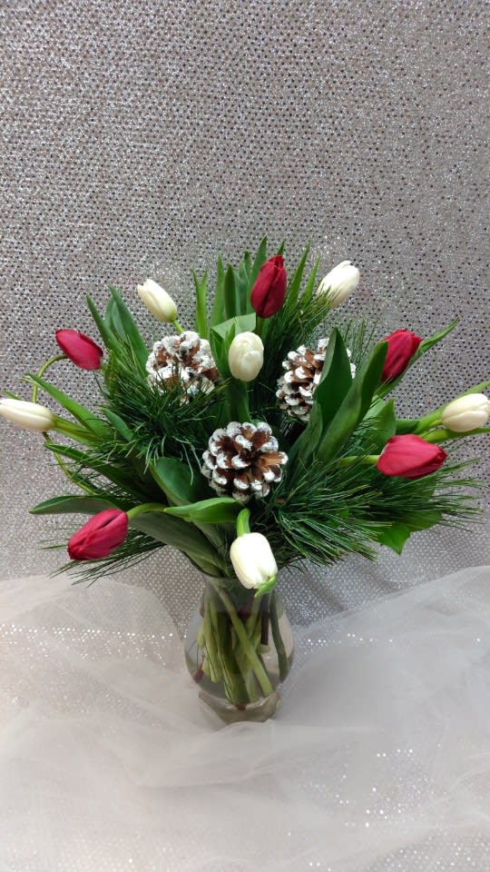 Red and white tulips arranged in a glass vase with pinecones