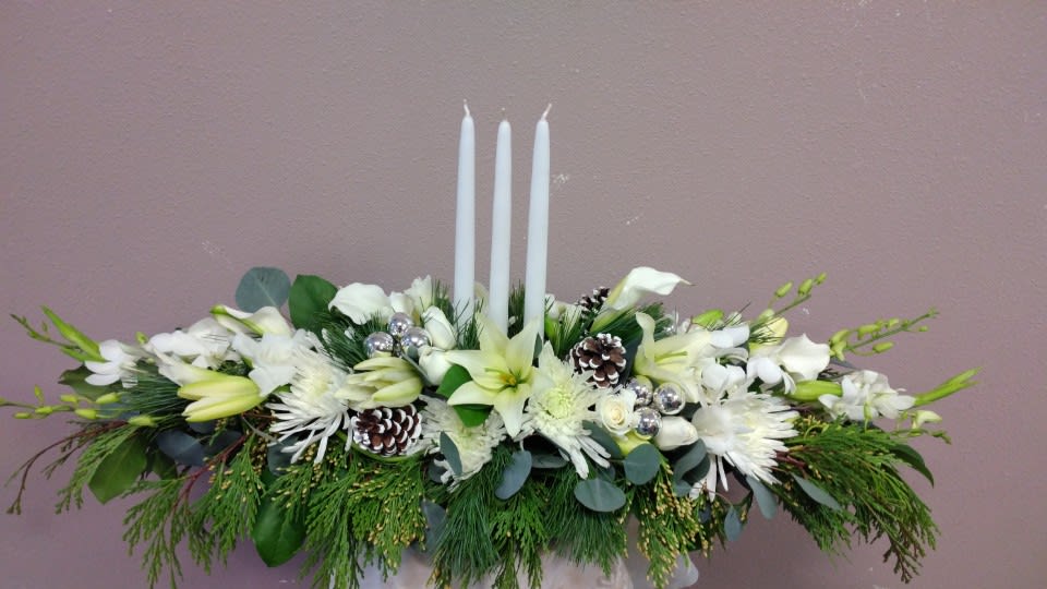 White floral centerpiece with three tall candles and pinecones