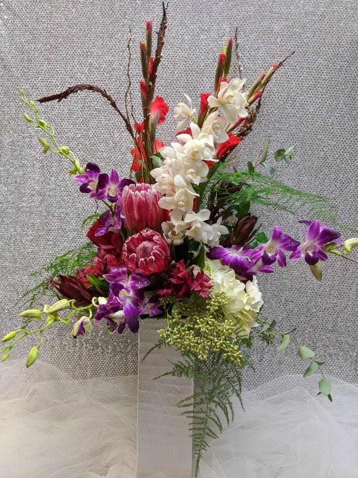 Tall floral arrangement with purple orchids, white orchids, and red tropical blooms in a white vase