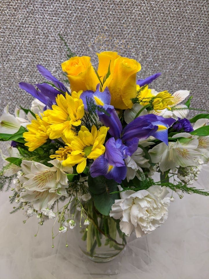 Bouquet of yellow roses, purple irises, and white flowers in a glass vase