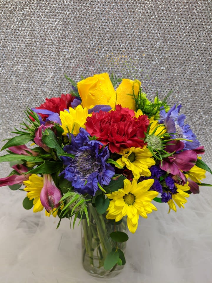 Colorful mixed bouquet in a clear glass vase with yellow, red, purple, and pink blooms