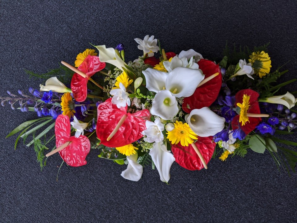 Long floral arrangement with red anthuriums, white calla lilies, and yellow daisies
