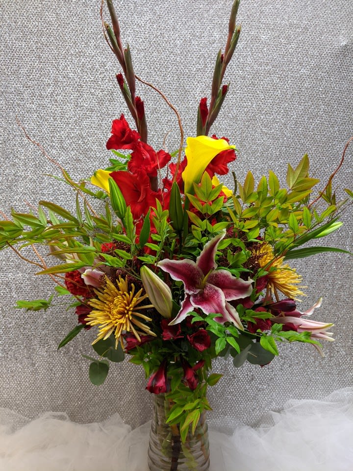 Tall mixed bouquet with red and yellow flowers in a glass vase