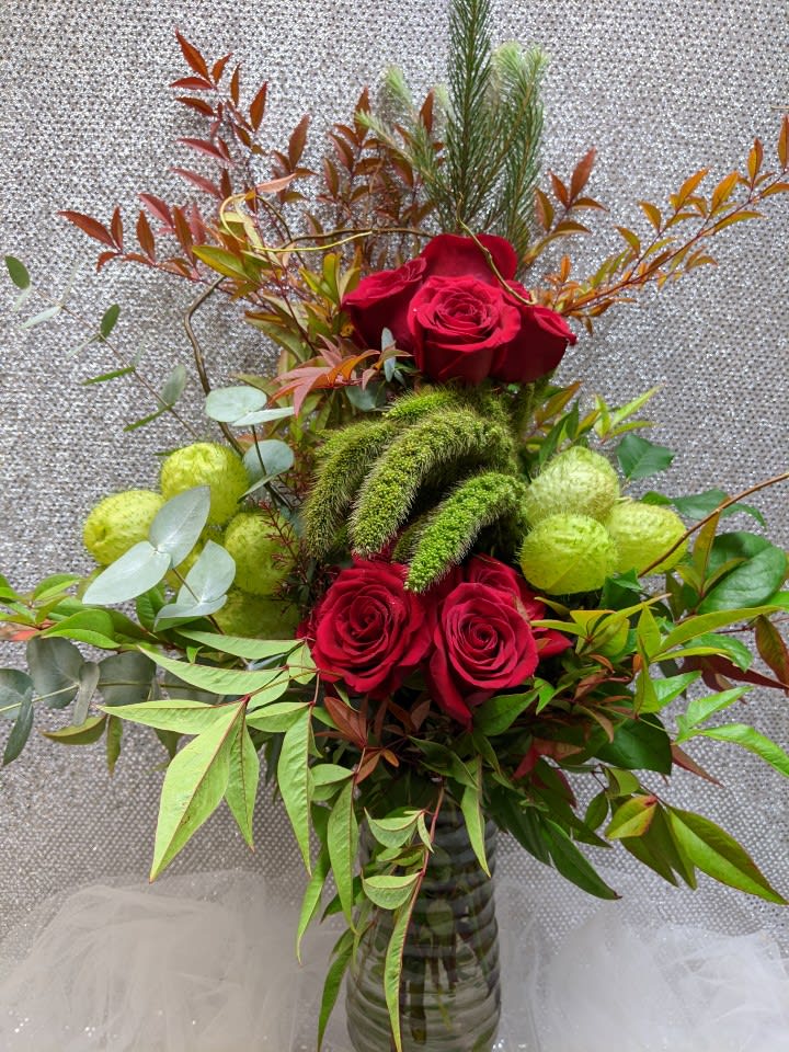 Red roses arranged in a glass vase with mixed greenery and green fuzzy accents