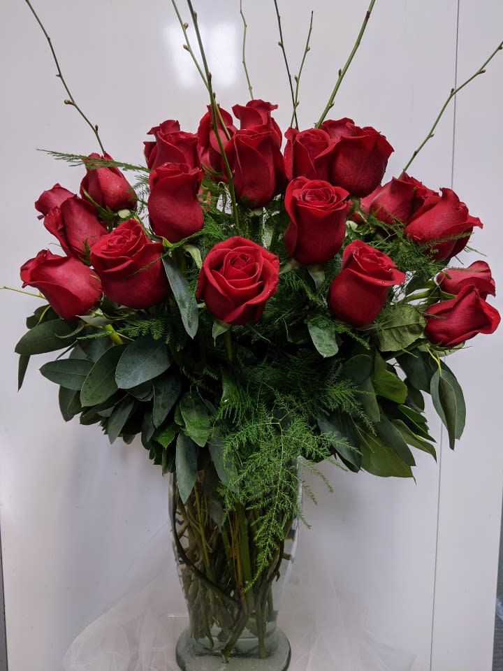 Red roses arranged in a clear glass vase with greenery