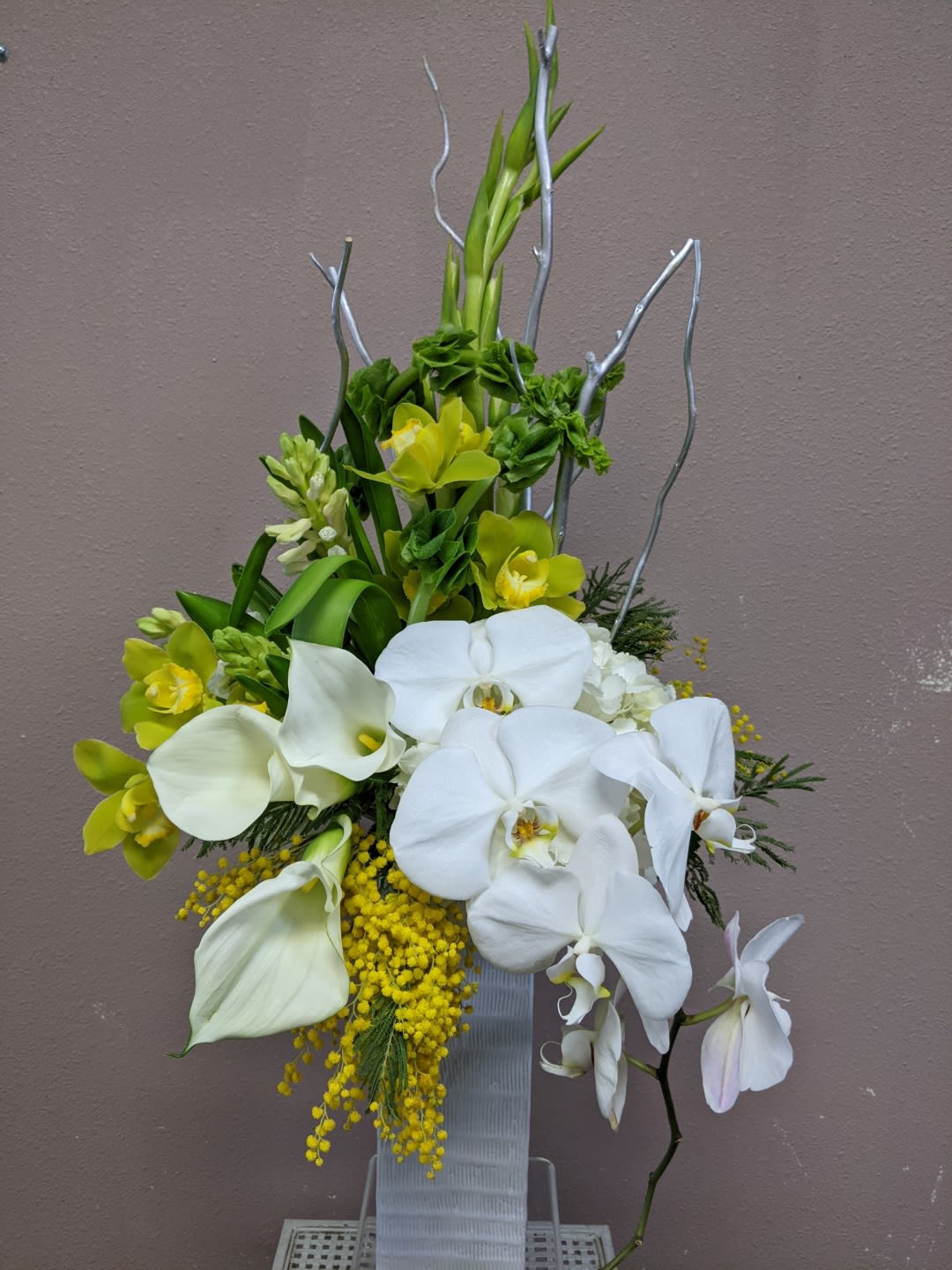 White orchids and calla lilies with yellow accents in a tall vase arrangement