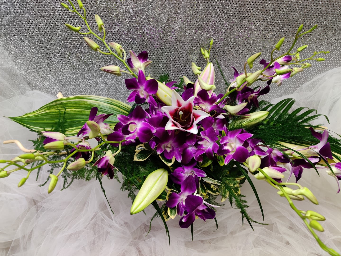 Purple orchid arrangement with white lilies and green foliage