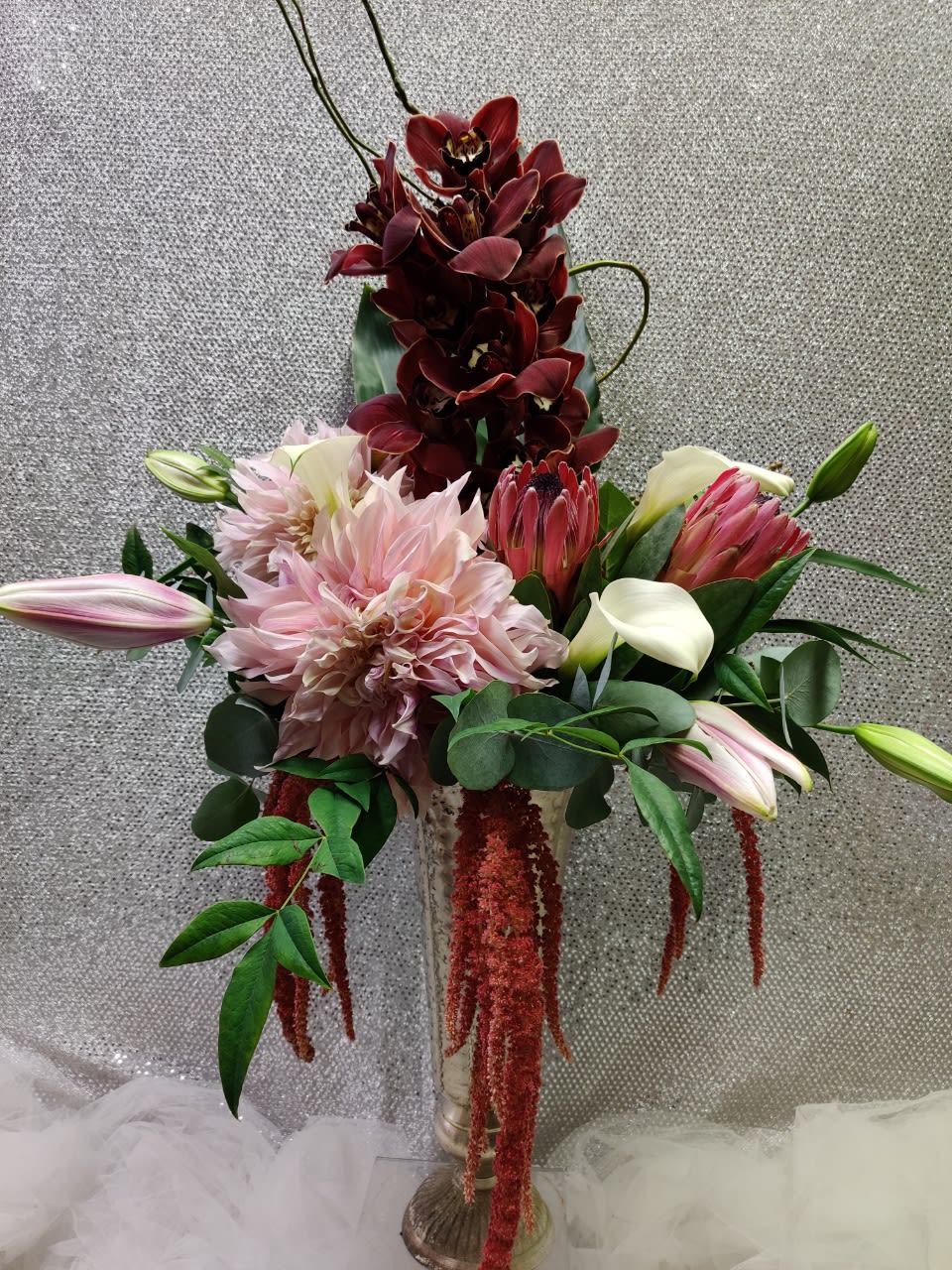 Tall floral arrangement with pink dahlias, burgundy orchids, and lilies in a glass vase