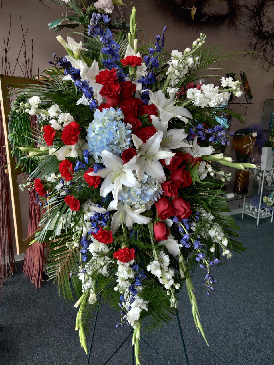 Large standing floral spray with red roses, white lilies, and blue flowers