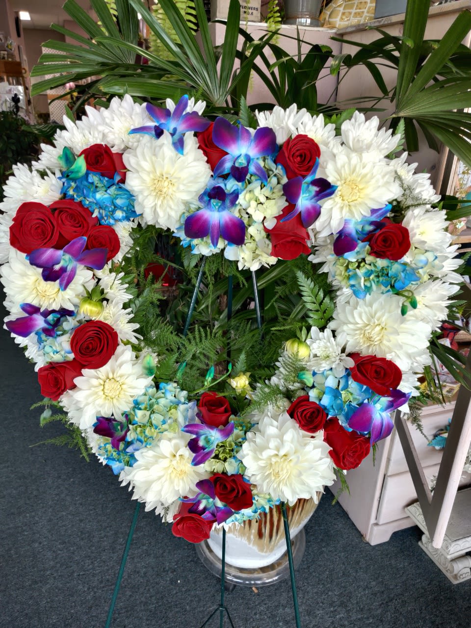 Heart-shaped floral wreath with red roses, white daisies, and blue orchids