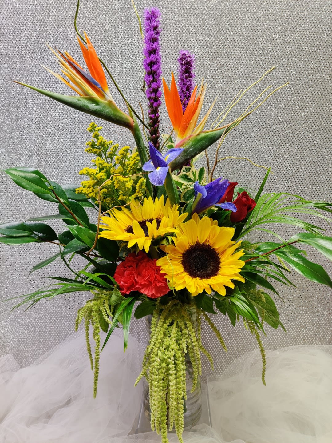 Tropical bouquet with sunflowers, bird of paradise, and purple spikes in a glass vase