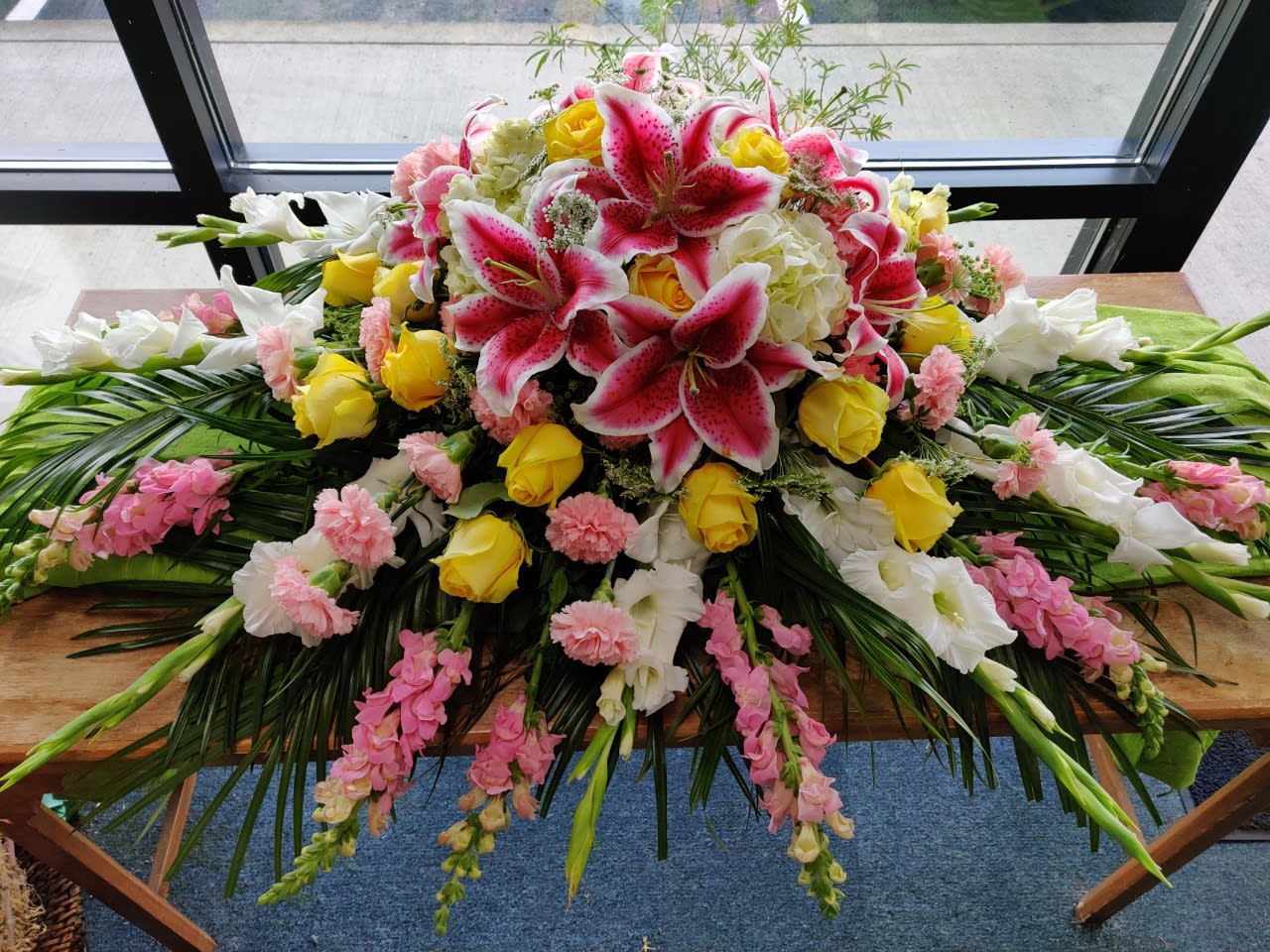 Large floral casket spray with pink lilies, yellow roses, and white blooms