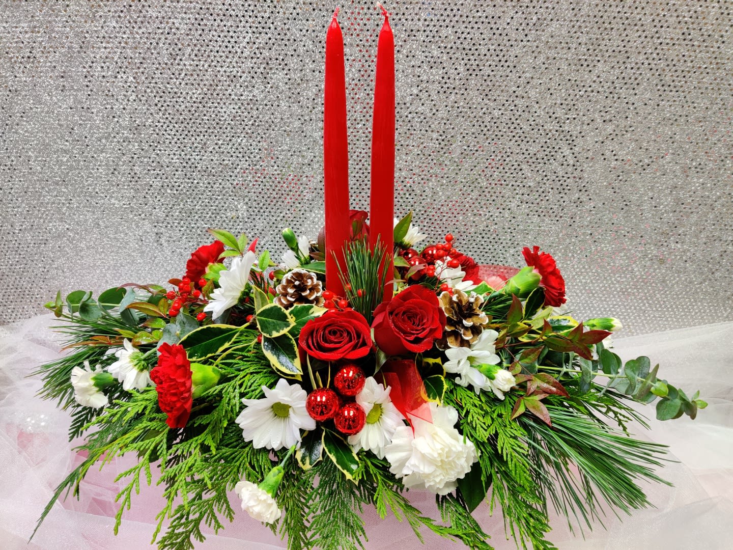 Red candles in a holiday floral centerpiece with roses and white blooms