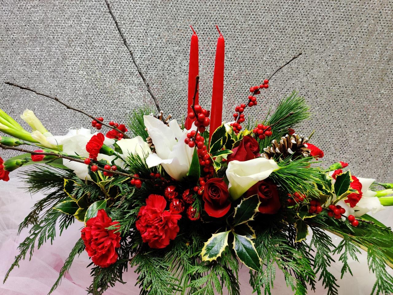 Holiday arrangement with red and white flowers, candles, and pinecones