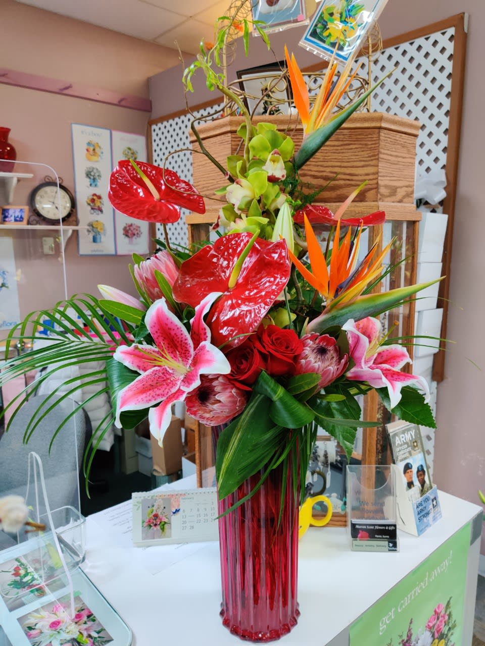 Tropical bouquet with red anthuriums, pink lilies, and orange bird-of-paradise in a red vase