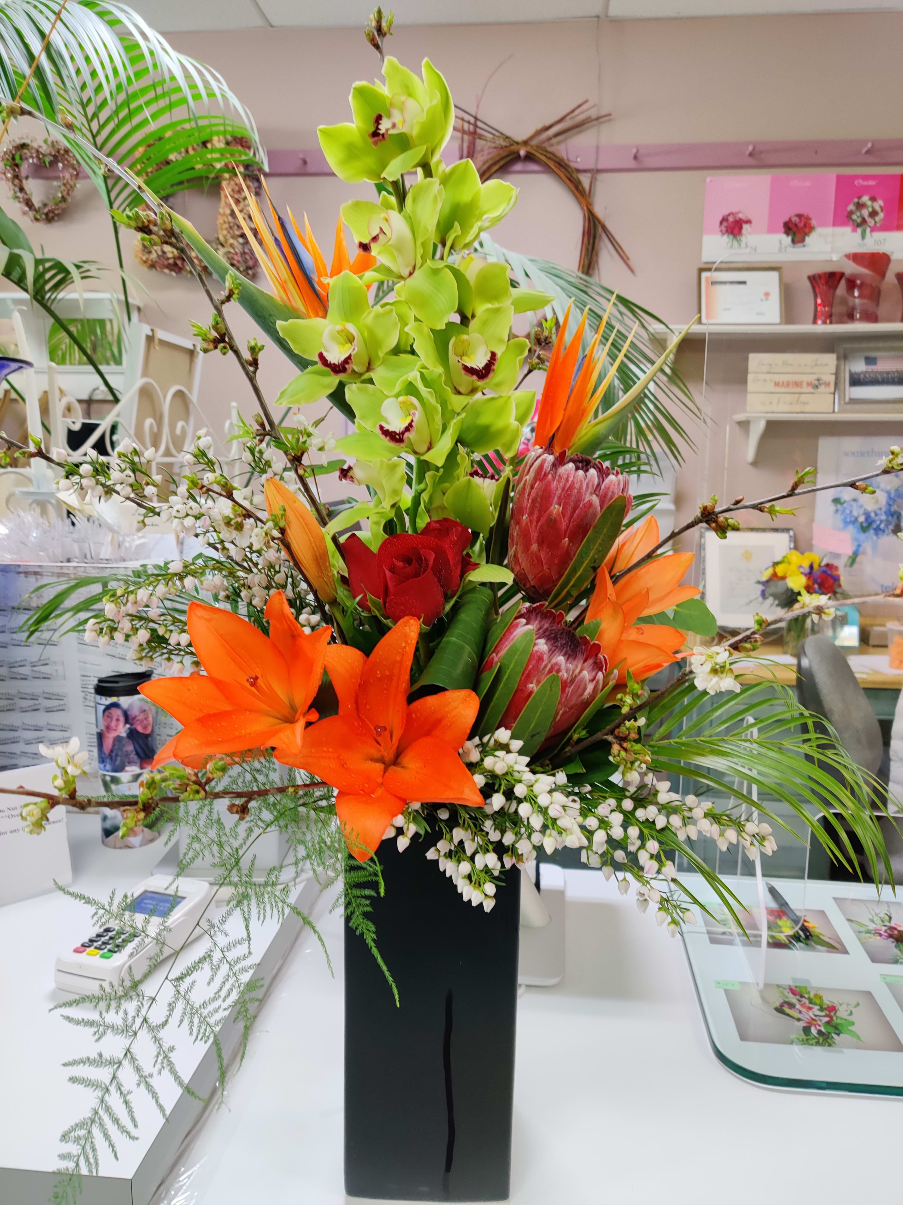 Tropical flower arrangement with orchids, lilies, and protea in a black vase