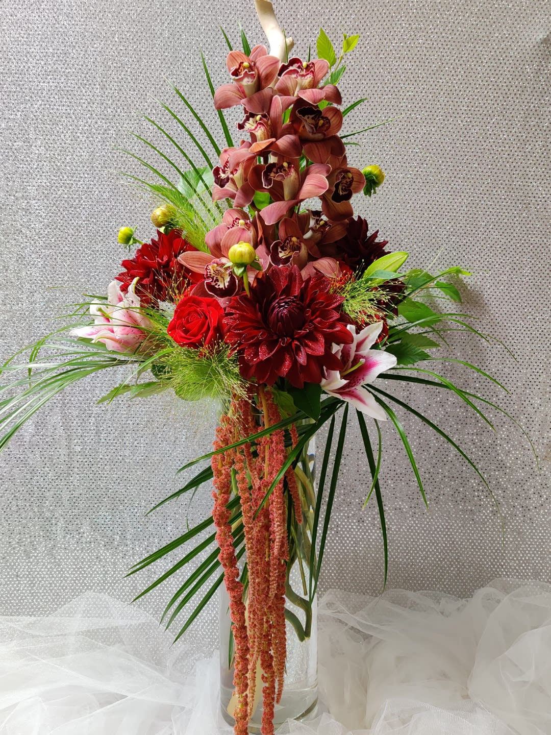 Tall floral arrangement with red and pink blooms in a clear glass vase