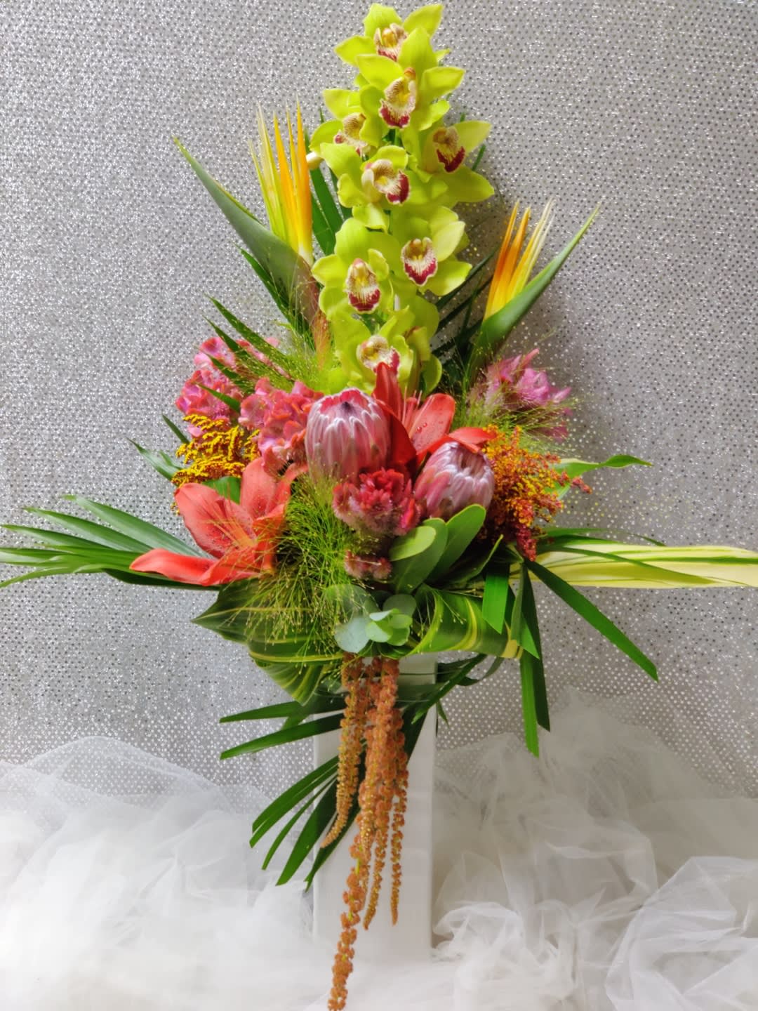 Tall tropical bouquet with green orchids and pink protea in a white vase