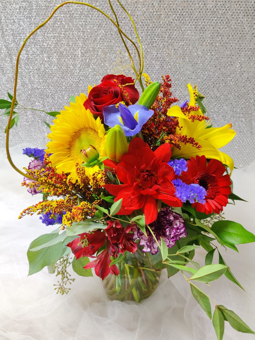 Bright mixed bouquet with red roses, sunflowers, and lilies in a glass vase