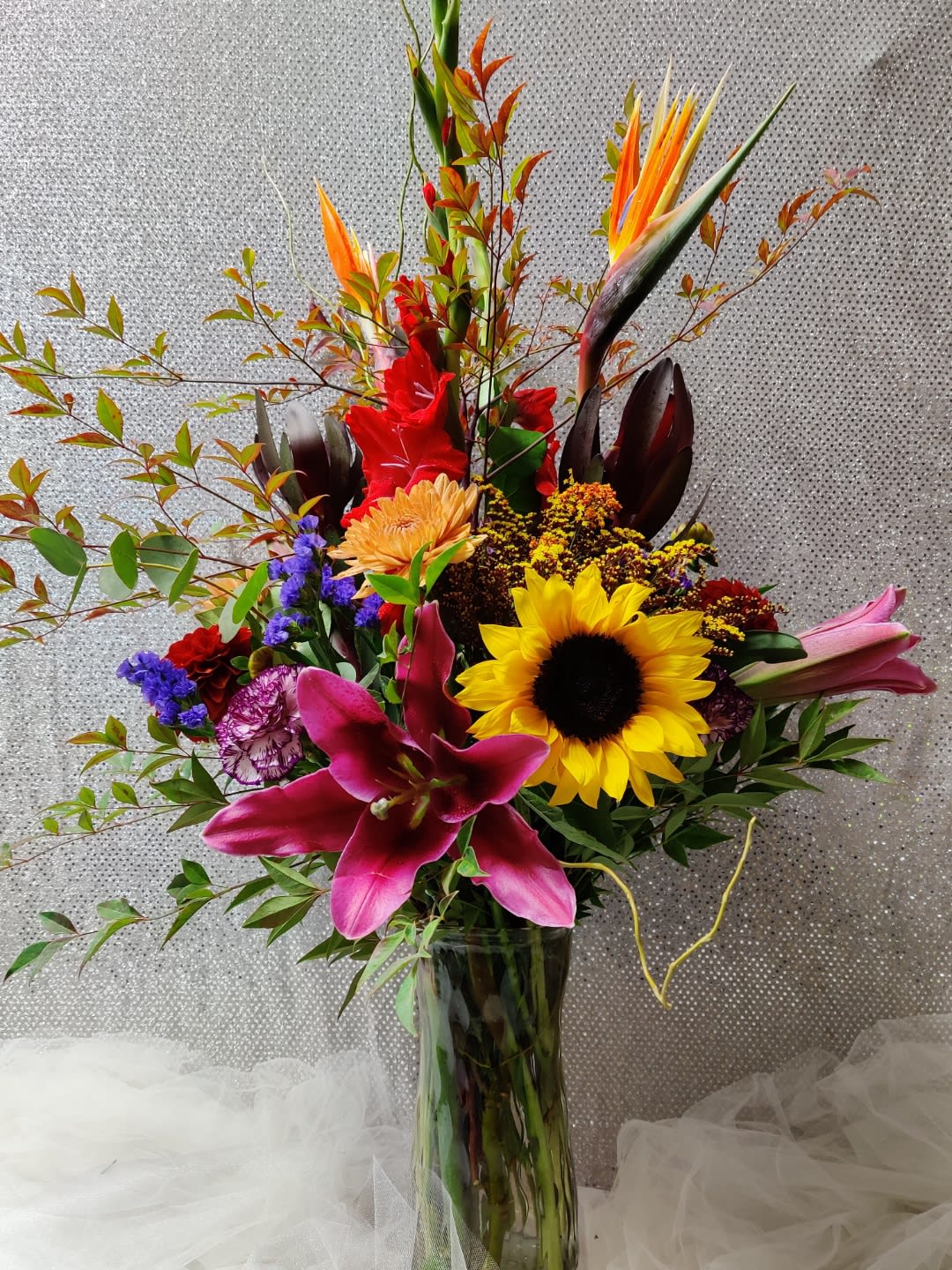 Tall mixed bouquet with sunflowers, lilies, and tropical blooms in a glass vase