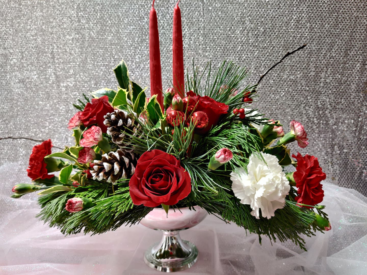 Christmas centerpiece with red roses, white carnations, and candles in a glass vase