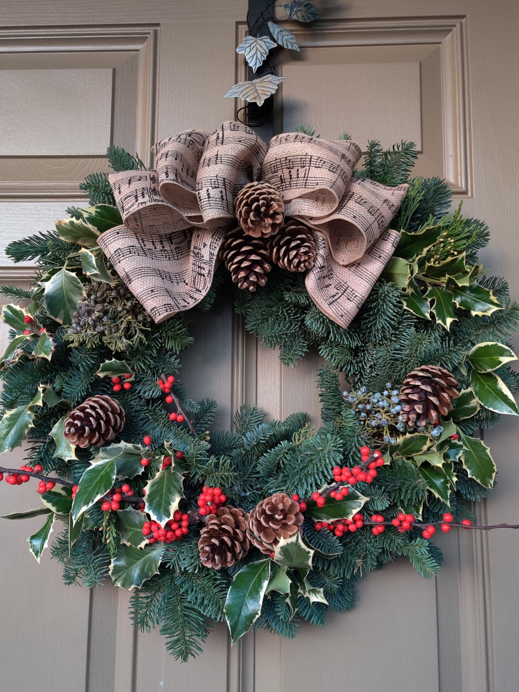 Holiday wreath with pine, holly, pinecones, and a music-note ribbon bow