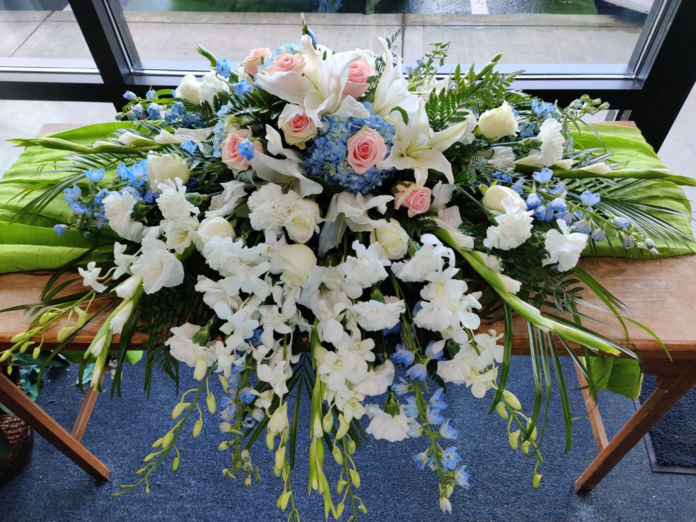 Large white floral casket spray with pink roses and blue accents