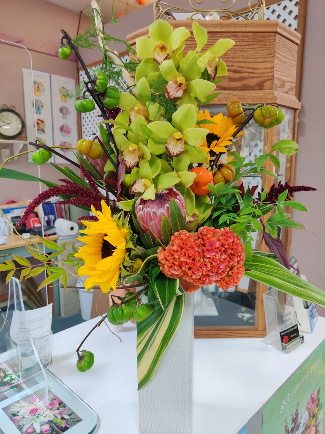 Tall mixed floral arrangement in a white vase with green orchids and sunflowers