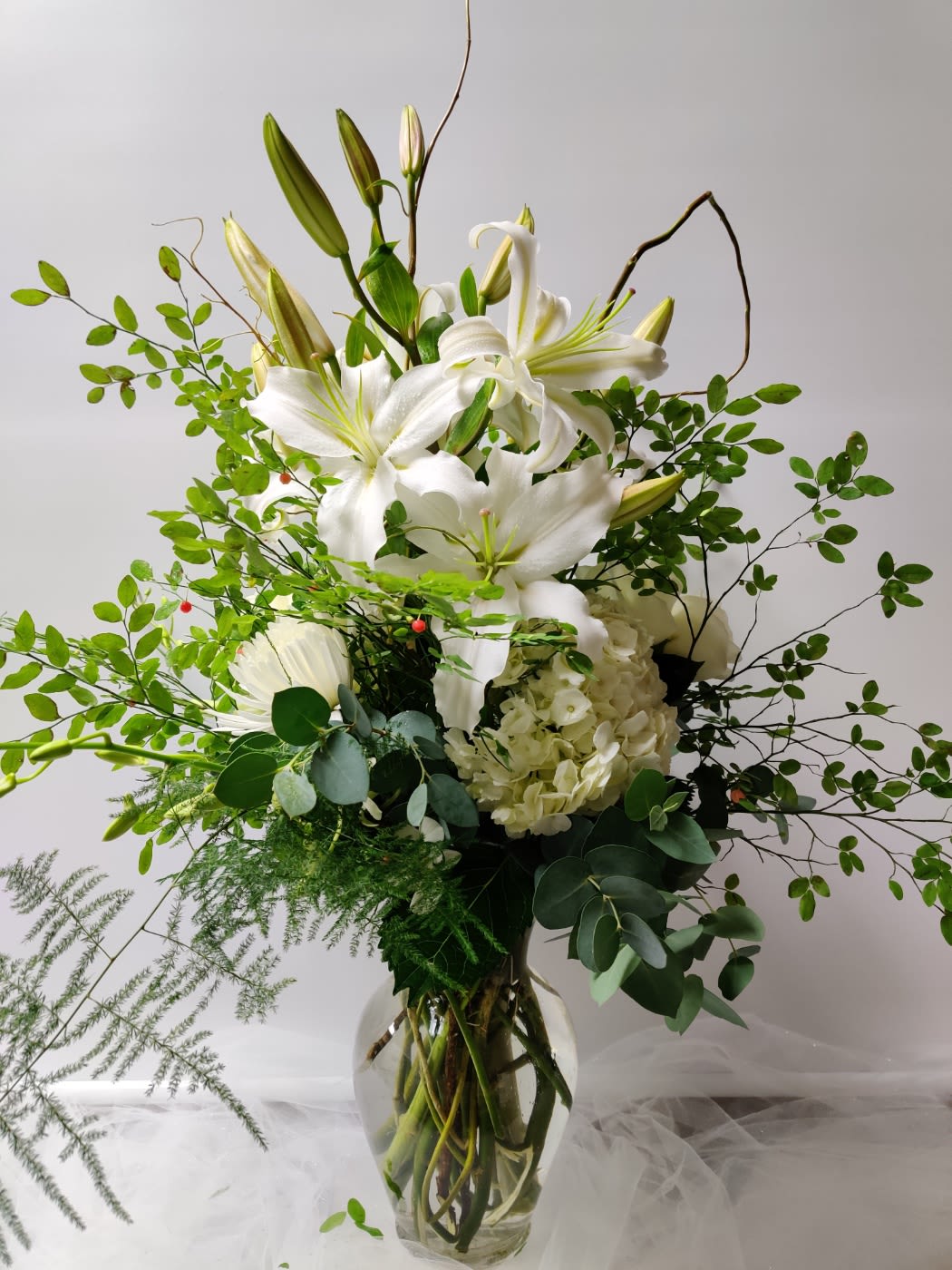 White lilies and hydrangea in a glass vase with airy greenery