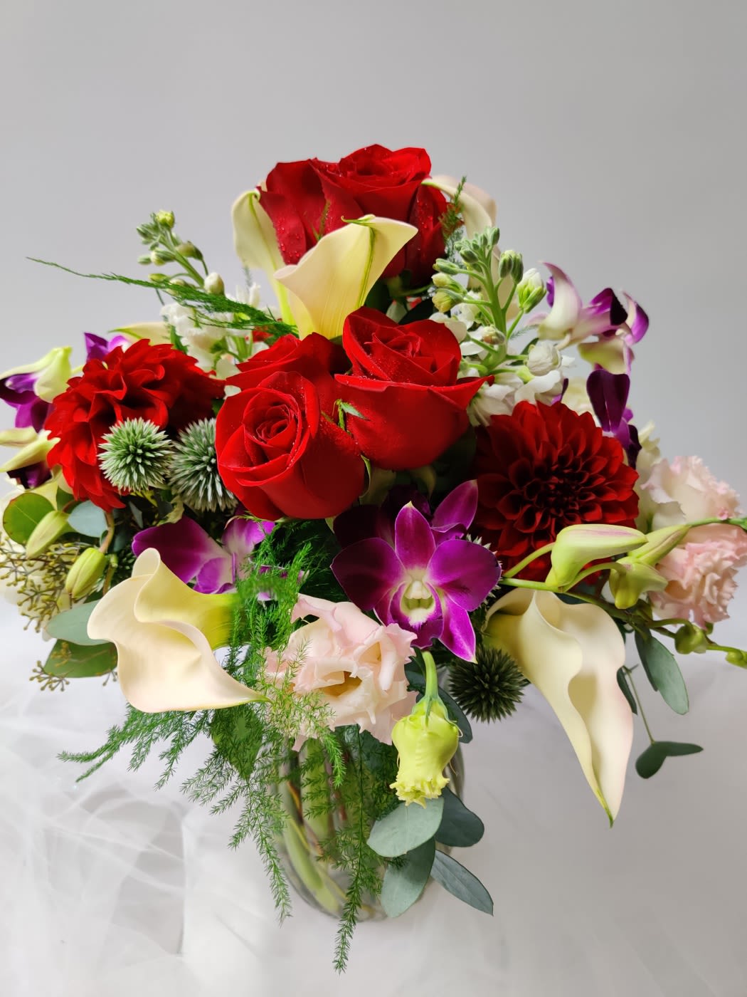 Bouquet of red roses, white calla lilies, and purple orchids in a vase